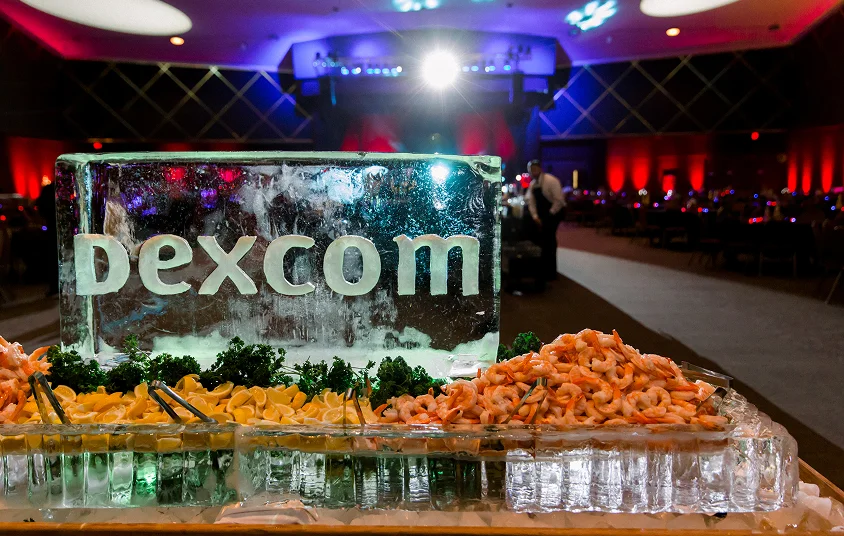 Corporate event seafood display with shrimp and lemons arranged around an ice sculpture centerpiece in a banquet hall.